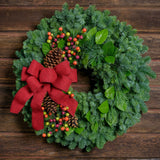 Holiday wreath with pine cones, faux autumn berries and a red linen bow on a base of noble, pine and salal greens on dark wood background