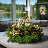 An arrangement made of noble fir, incense cedar, and white pine with burgundy ball clusters, Austrian pinecones, plum and cream berry pods with leaves, and two fluffy owls sitting on a counter..