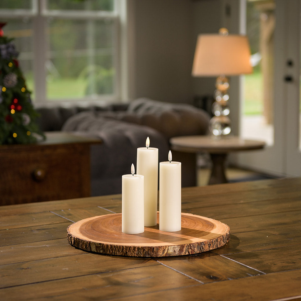 Set of 3 ivory LED candles with a 360 degree flame on wood round sitting on a wood table.