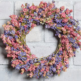 10” dried larkspur wreath with mixed pink and lavender larkspur on a white brick background.