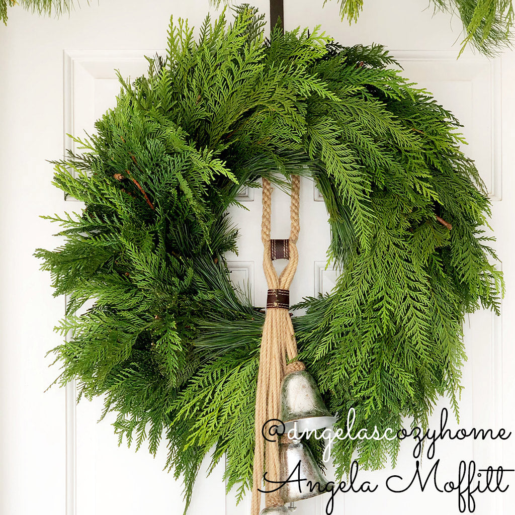 Christmas wreath with cedar and pine and an added decorative bells ornament hanging on a front door.