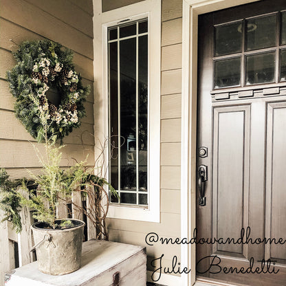 Holiday wreath made of noble fir, incense cedar, white pine, and bay leaf with faux white berries and leaves, and Australian pine cones hanging on a front porch