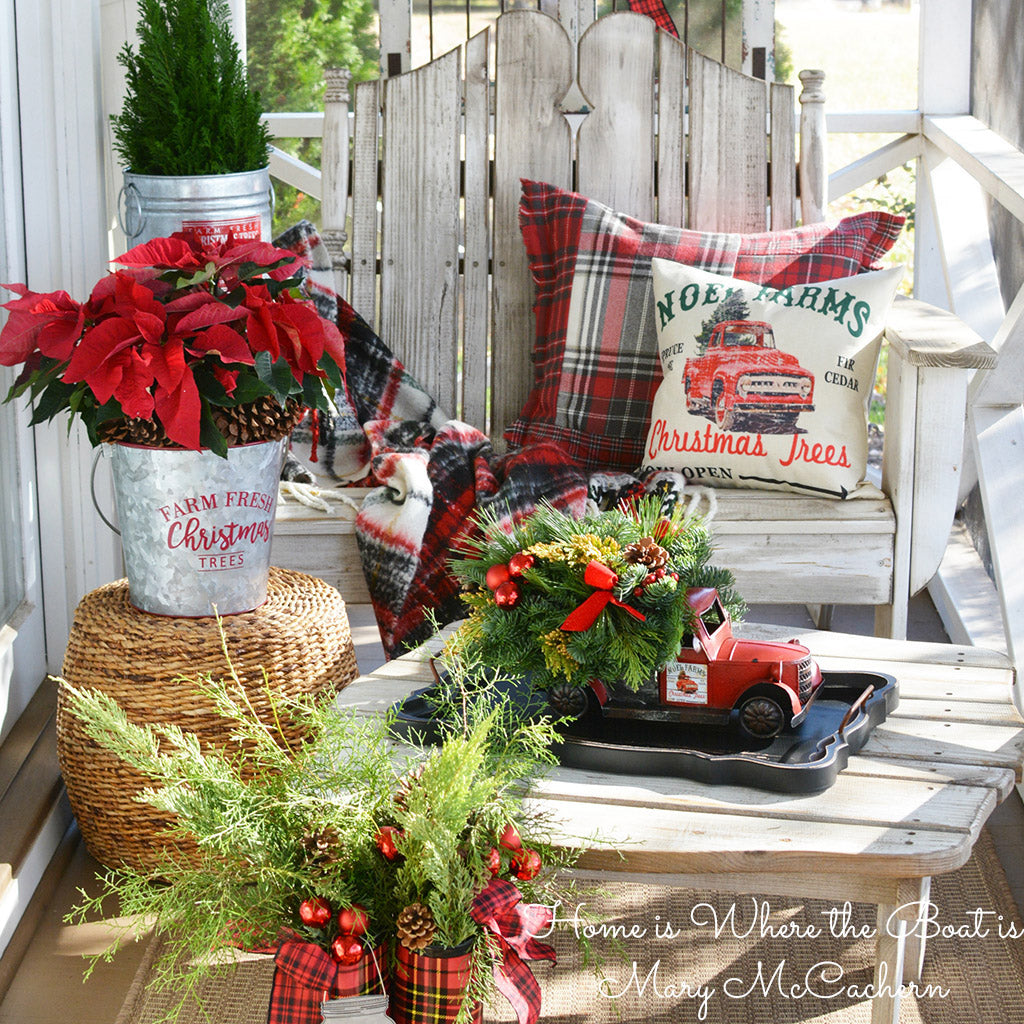 Fresh greens, pinecones, red ball & berry clusters, red velvet bow tucks in a metal truck with removable “Noel Farms” magnets on a porch. 