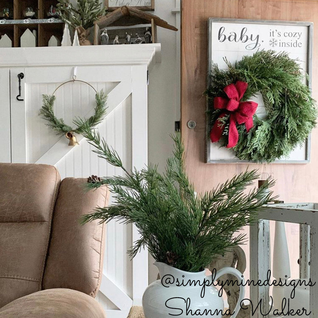 Fresh Evergreen Christmas wreath with cedar and pine and a brushed red bow hanging on a light wood door.