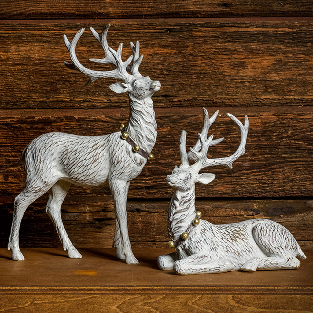 Set of 2 off-white reindeer with jingle bell collars with a dark wood background.