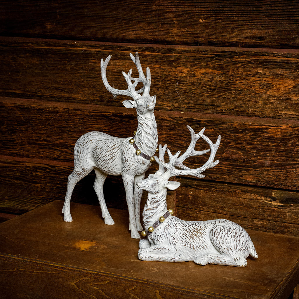 Set of 2 off-white reindeer with jingle bell collars with a dark wood background.