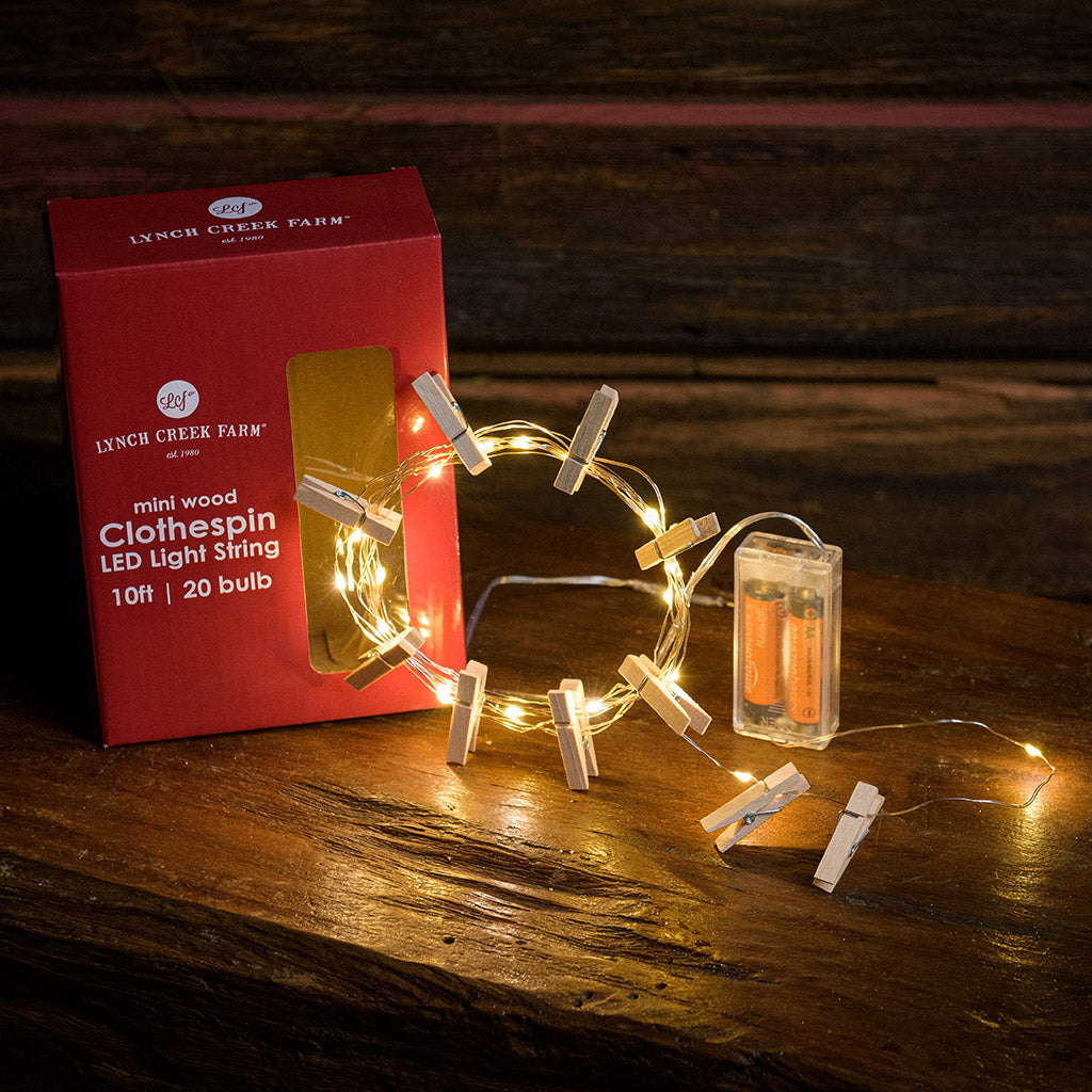 10-foot strand of white lights and mini wood clothespins and their packaging with a dark wooden background.