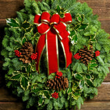Christmas wreath made of variegated holly, noble fir, incense cedar and juniper with ponderosa pine cones, faux red berry clusters and a red velveteen with gold back bow up close