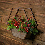 Centerpiece with noble fir, cedar, and pine with 2 ponderosa pine cones, 2 Australian pine cones, 1 red ball cluster, 4 red berry branches, 2 red plaid bow tucks, and a hexagon metal and wooden container mounted on a wooden wall