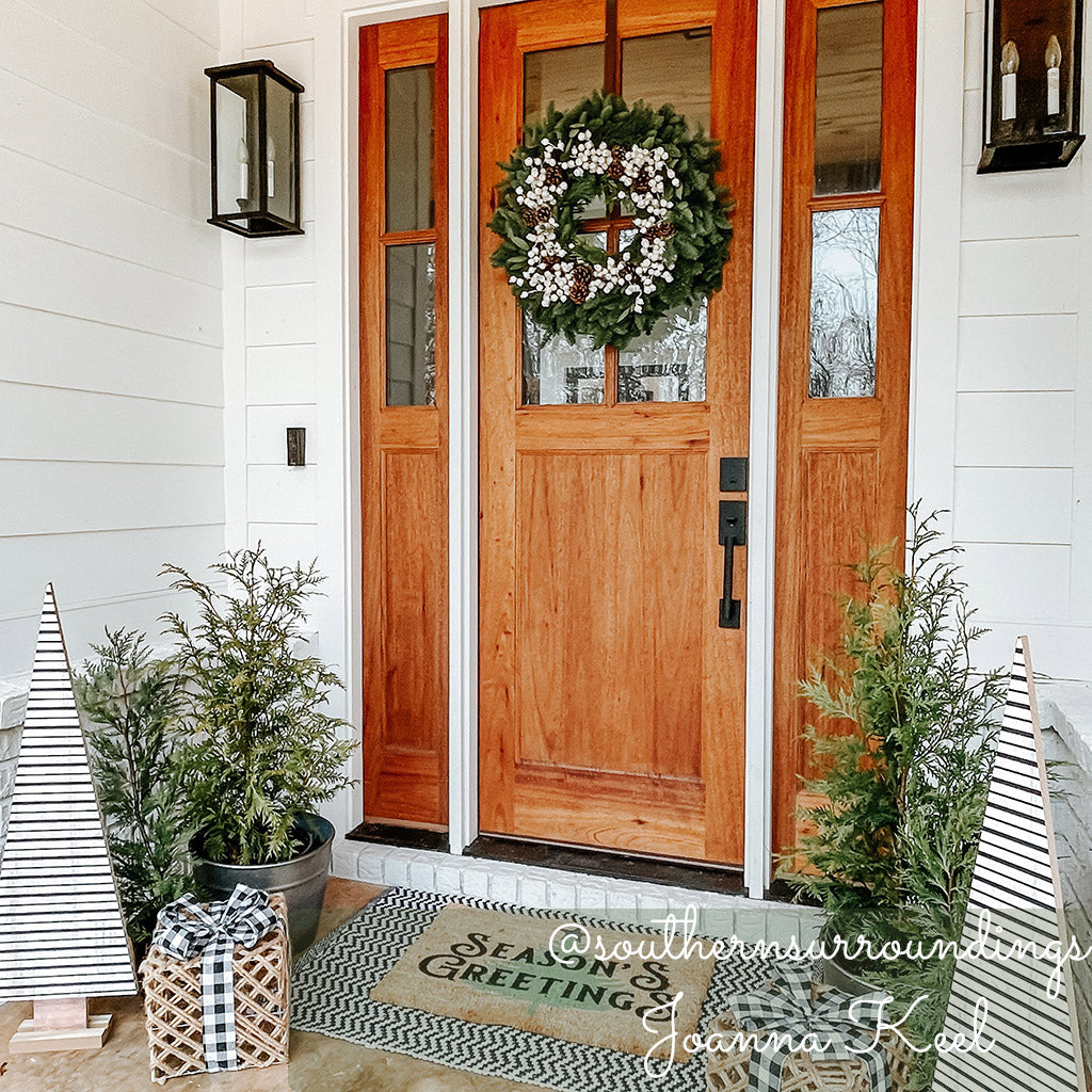 Holiday wreath made of noble fir, incense cedar, white pine, and bay leaf with faux white berries and leaves, and Australian pine cones hanging on a front door