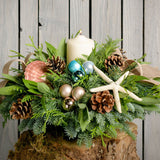 Fresh centerpiece with seashells, sea star, aqua balls, pine cones, burlap bow and a white pillar candle close up