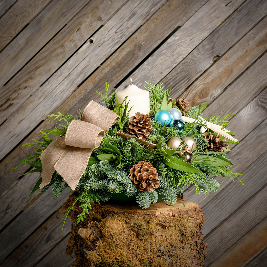 Fresh beach themed centerpiece with a burlap bow and a white pillar candle on a tree stump in front of wooden wall