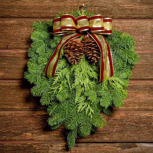 Christmas Swag made with fir cedar juniper pine cones and gold and burgundy bow on a wood background.