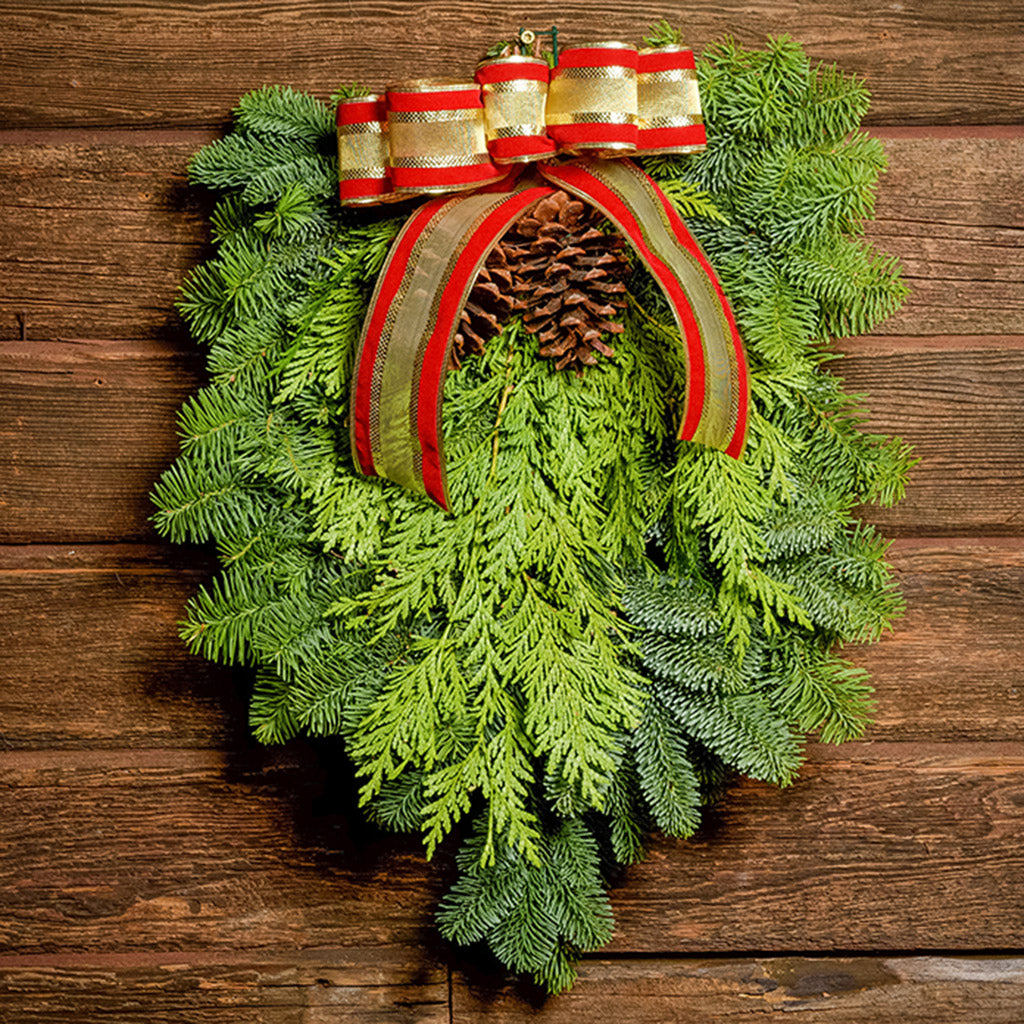 Christmas Swag made with fir cedar juniper pine cones and gold and red bow on a wood background.