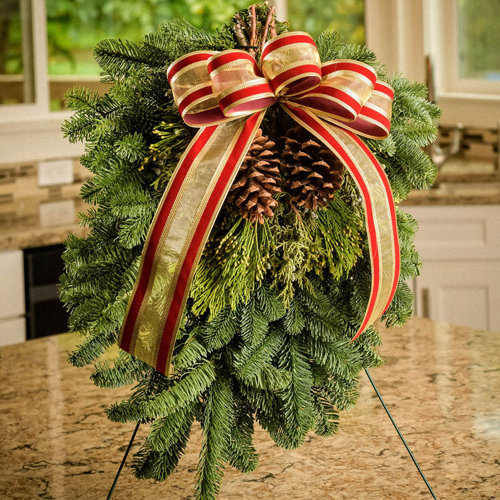 Christmas Swag made with fir cedar juniper pine cones and gold and red bow held up with an easel sitting on a counter.
