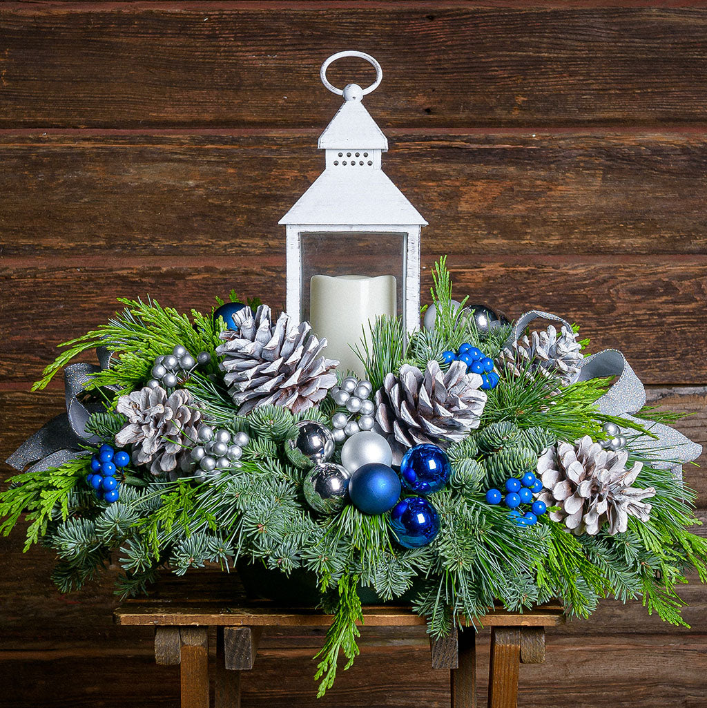 Evergreen centerpiece with white pine cones, silver and blueberries and balls, silver glitter bow and a white LED lantern