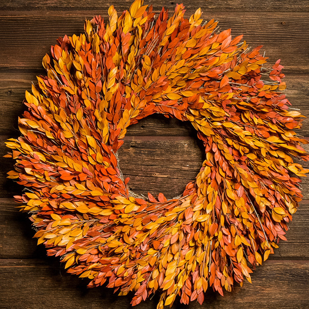 22” wreath made with a blend of yellow and orange myrtle on a dark wood background.