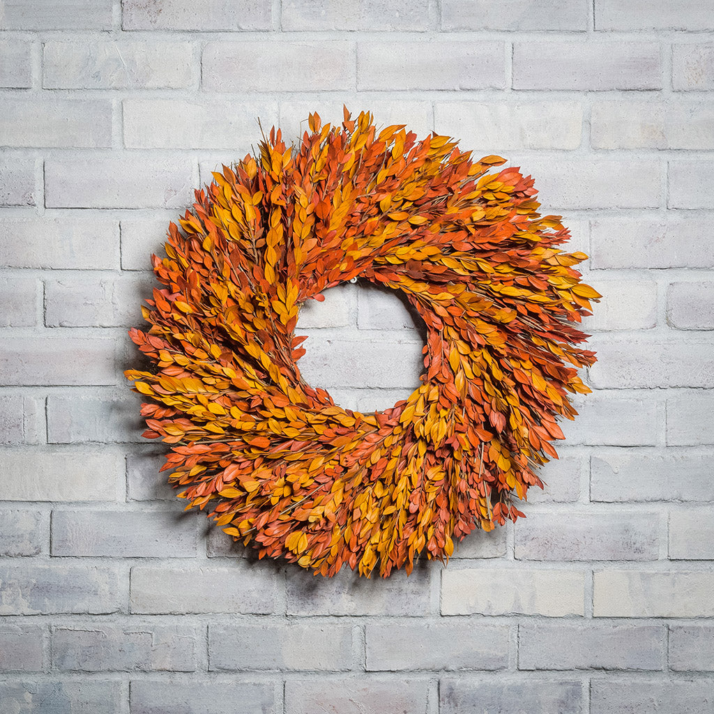 22” wreath made with a blend of yellow and orange myrtle on a white brick background.