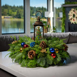 An arrangement made of noble fir, incense cedar, and white pine with Austrian pinecones, red, blue, and gold berry and ball clusters, and a musical Christmas tree spinning in a lantern globe sitting on a counter.