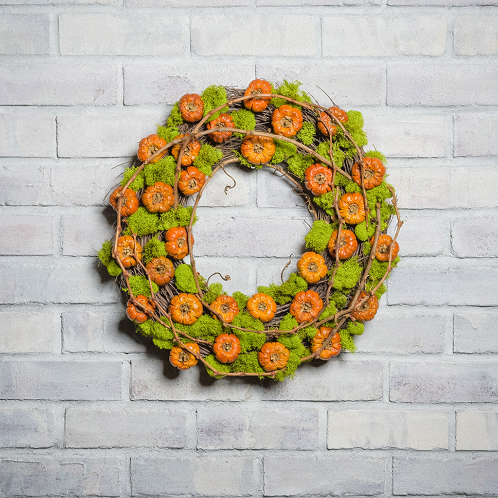 18" natural wreath made of real, dried cherry pumpkins and contrasting green reindeer moss. and grapevine accents on a white brick background. 