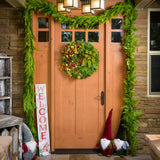 A holiday wreath of noble fir and western red cedar with faux pumpkins, faux acorns, sage accents, leaf and berry accents, 2 copper ball clusters, 2 bright green ball clusters, 3 gold pinecones, 4 Australian pinecones, 1 ponderosa pinecone, and a brushed green linen bow on a front door.