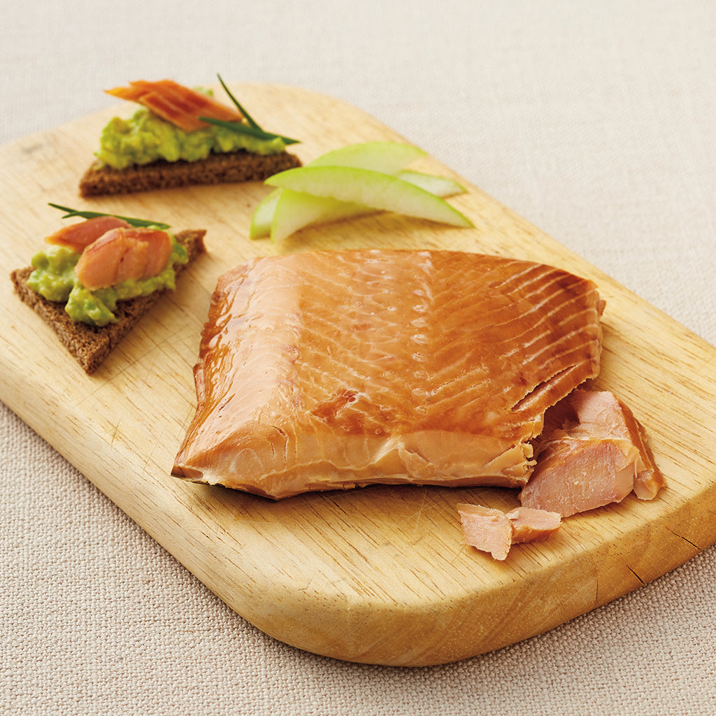 Smoked salmon on toast with a green paste  and pears sitting on a wooden cutting board.