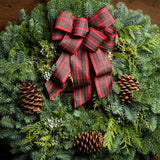 Christmas wreath of noble, cedar, juniper, pine cones and a red plaid bow close up