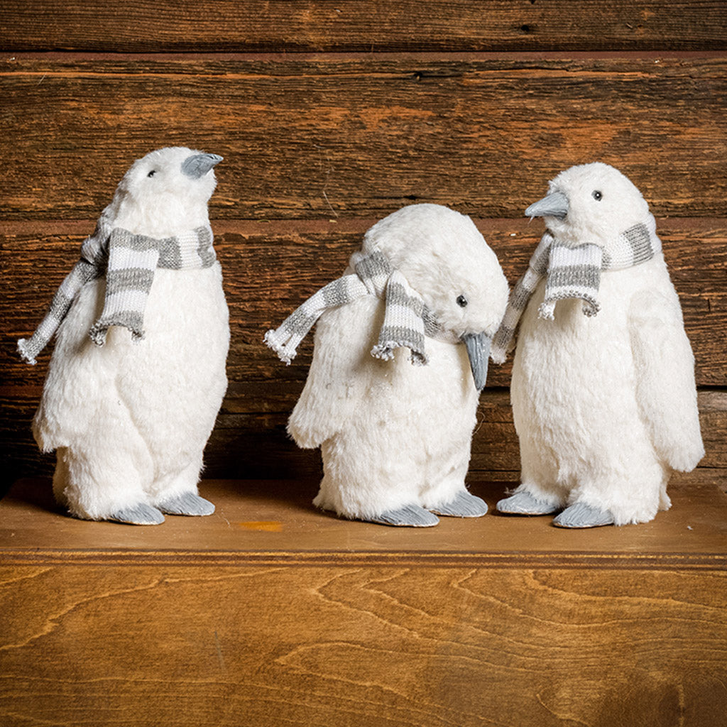 Set of 3 white penguins with gray and white scarves standing on a wood table with a dark wooden background.