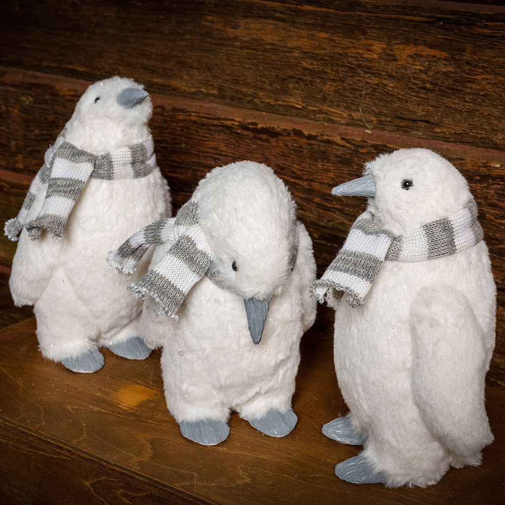 Set of 3 white penguins with gray and white scarves standing on a wood table with a dark wooden background.