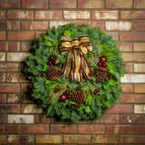 Holiday wreath made of noble fir, incense cedar, juniper, and salal leaves with ponderosa pine cones, faux burgundy berry clusters, ball clusters, and burgundy bow hanging on a brick wall