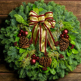 Holiday wreath made of noble fir, incense cedar, juniper, and salal leaves with ponderosa pine cones, faux burgundy berry clusters,  ball clusters, and burgundy bow close up