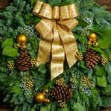 Holiday wreath made of noble fir, incense cedar, juniper, and salal leaves with ponderosa pine cones, faux gold berry clusters, ball clusters, and a gold bow close up