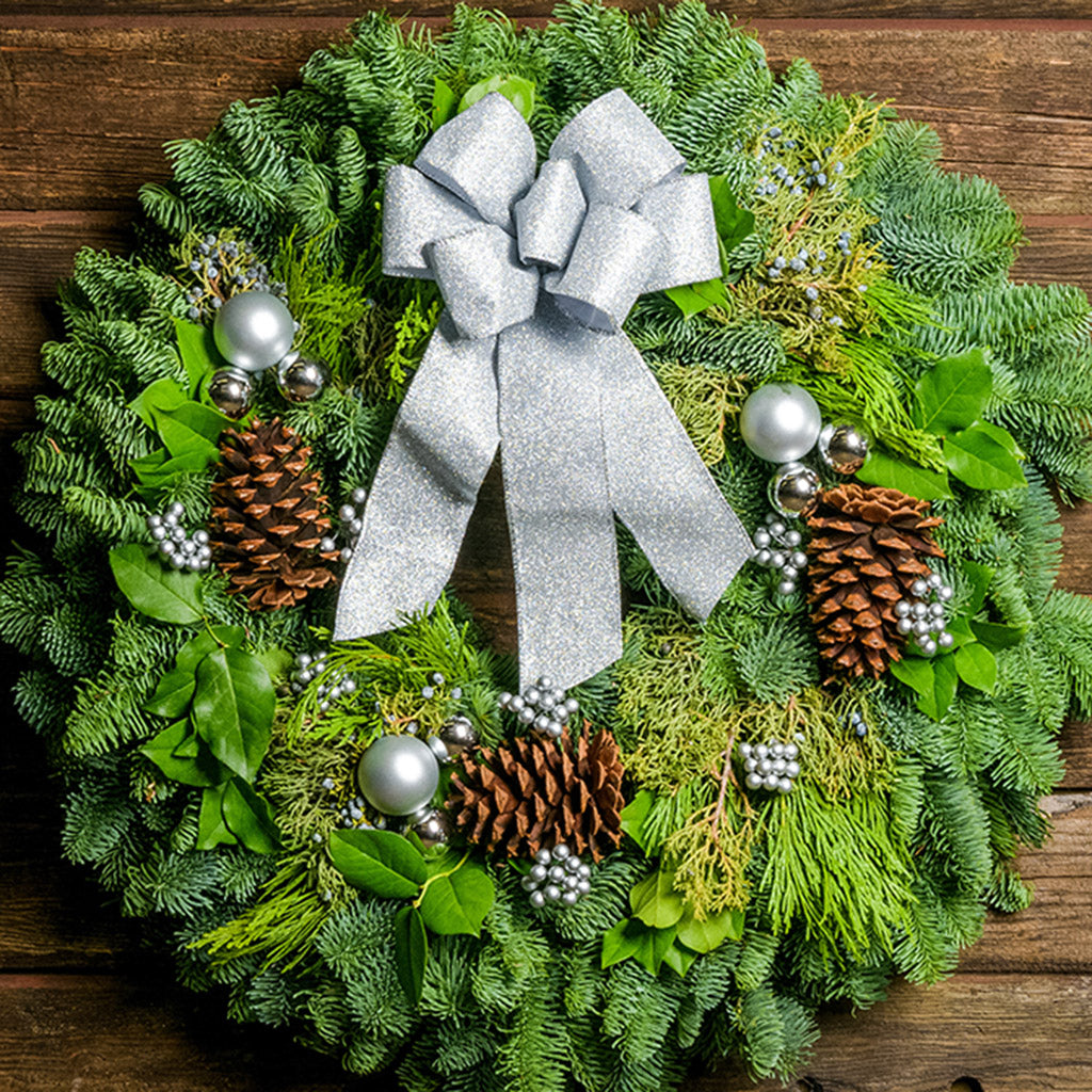 Holiday wreath made of noble fir, incense cedar, juniper, and salal leaves with ponderosa pine cones, faux silver berry clusters,  ball clusters, and a silver bow up close