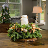 Centerpiece made of noble fir, incense cedar, and white pine with Australian pine cones, gold and silver ball clusters, silver berry clusters, and a lighted holiday glass jar on a wooden table