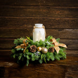 Centerpiece made of noble fir, incense cedar, and white pine with Australian pine cones, gold and silver ball clusters, silver berry clusters, and a lighted holiday glass jar on a wooden table against a wood wall