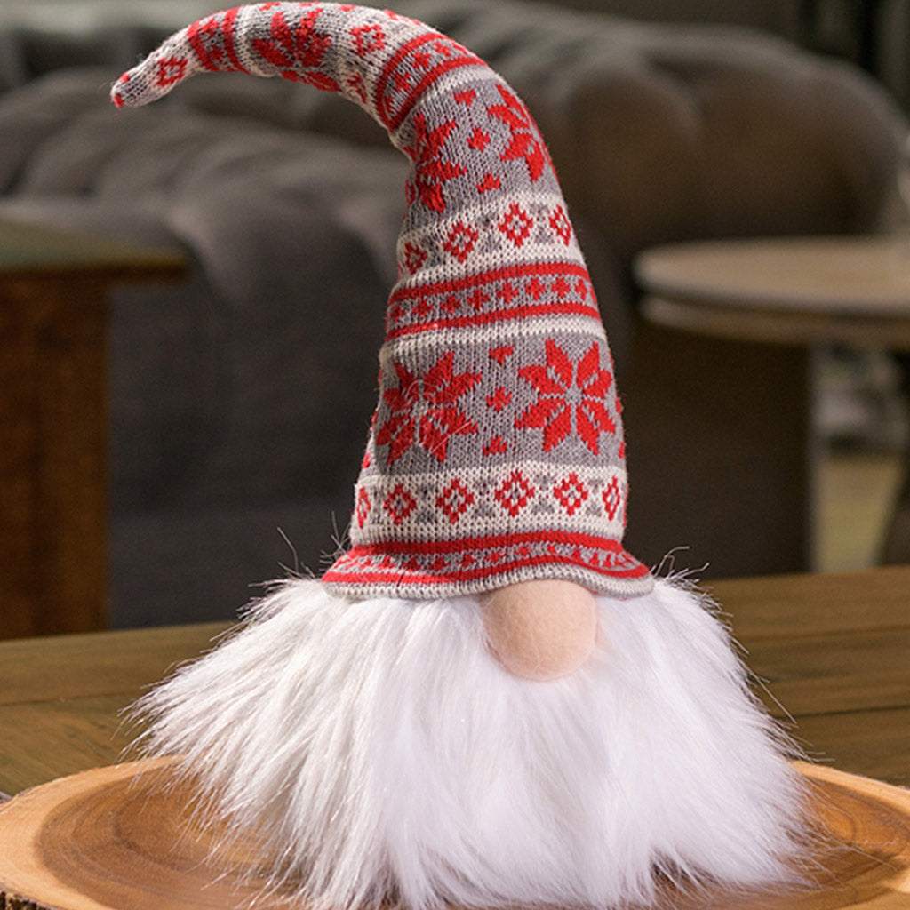Bearded light up gnome with nose sticking our from under the red, gray, and white Nordic style pointy sweater hat  sitting on a wood round on a table. 
