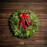 Christmas wreath of noble, cedar, juniper and salal with pine cones, red bow with gold edges and red berry clusters with a wood background.