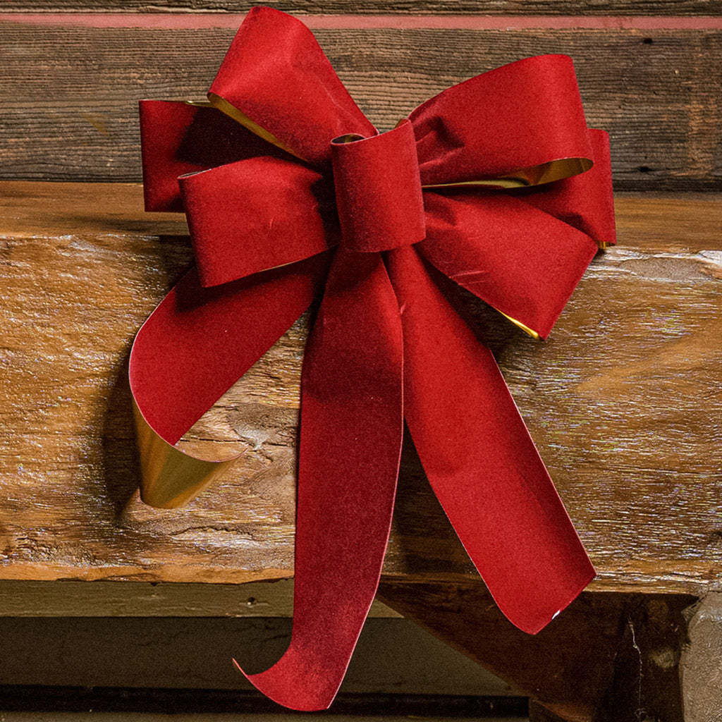 Red with shiny gold back bow shown sitting on a wood bench with a dark wood background.