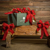 6 Red with shiny gold back bows shown with a green shipping box sitting on a wood bench with a dark wood background.