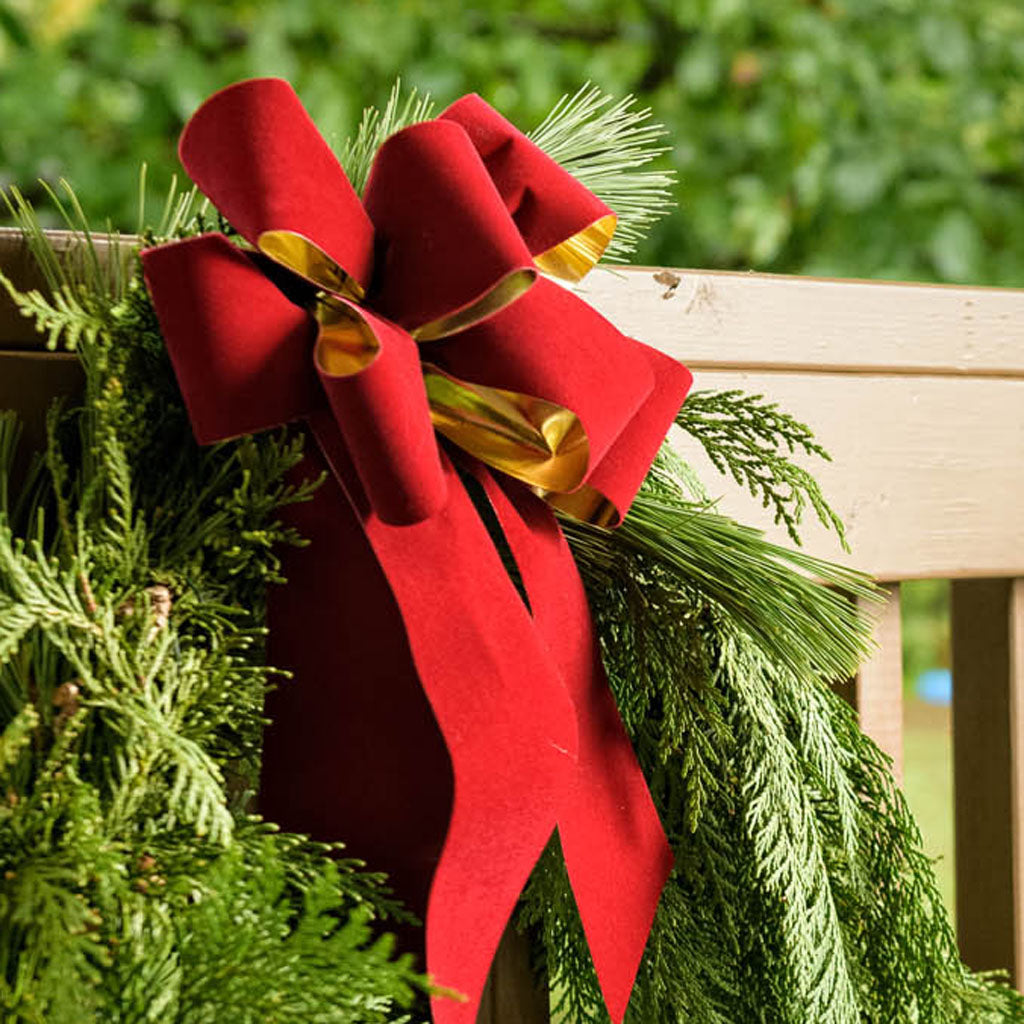 Gold backed red velveteen bow on garland on a wooden railing