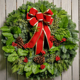 Christmas wreath of noble, cedar, juniper and salal with pine cones, red bow with gold edges and red berry clusters close up