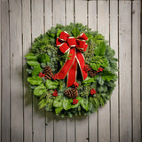 Christmas wreath with pine cones, red bow with gold edges and red berry clusters close up on wood plank background