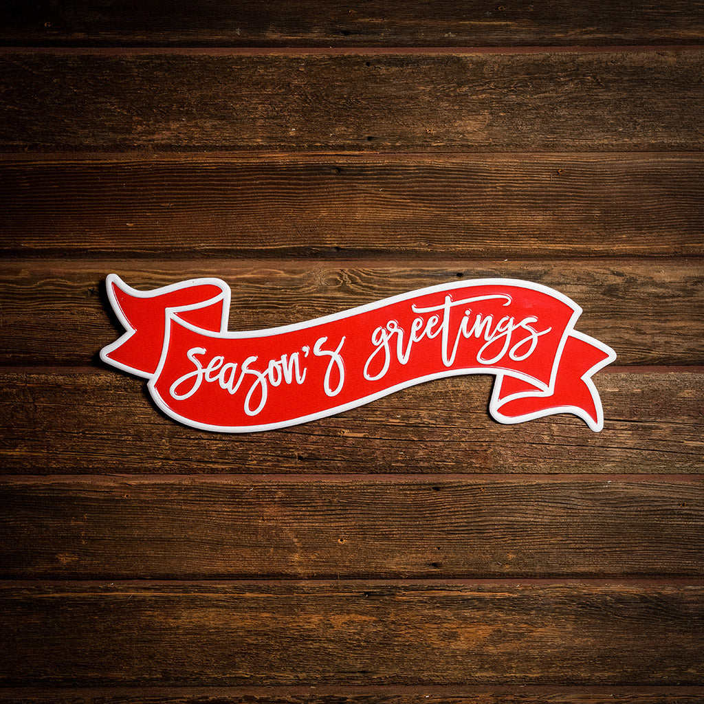 24" red and white metal Season's greetings sign on a dark wooden background.
