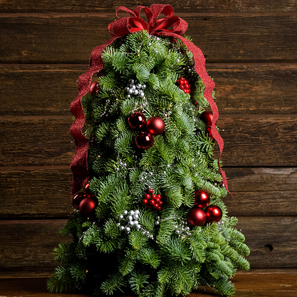 Tabletop tree of noble fir, red ball clusters, red berry clusters, silver berry clusters, a strand of metallic silver pearl garland and a red glittery ribbon close up