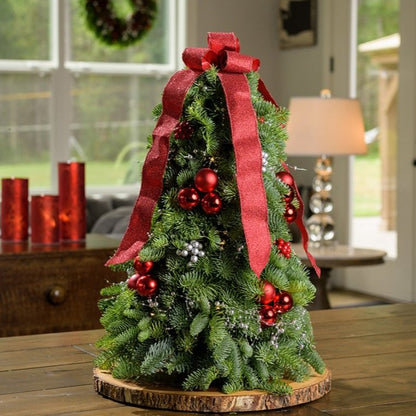 Tabletop tree of noble fir, red ball clusters, red berry clusters, silver berry clusters, a strand of metallic silver pearl garland and a red glittery ribbon on a wooden table