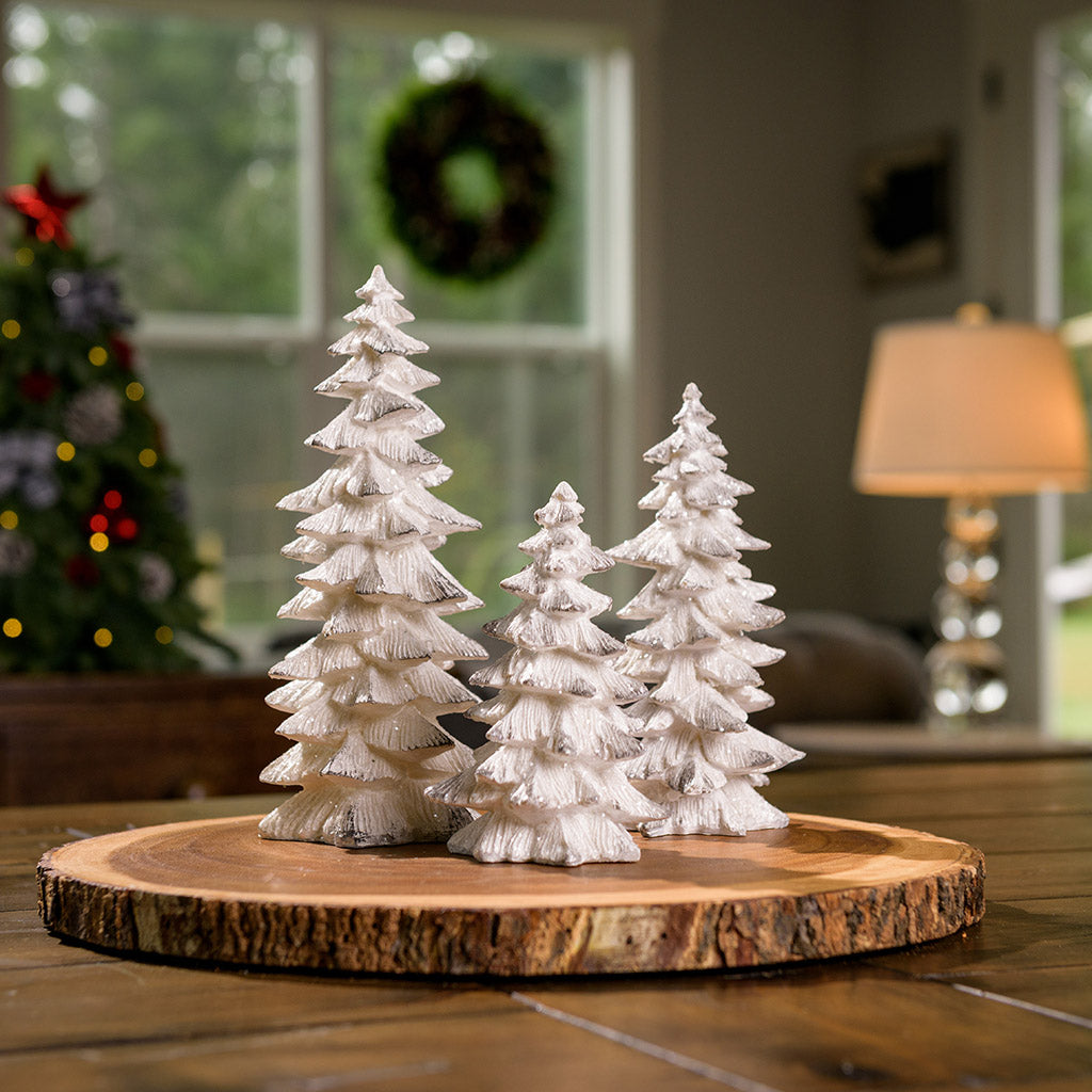 Set of 3 trees that are painted white with silver bough tips and covered in beautiful glitter sitting on a wood round.