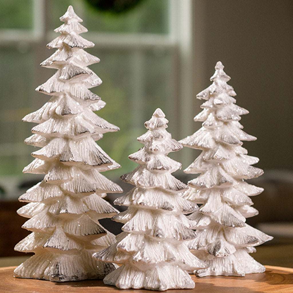 Set of 3 trees that are painted white with silver bough tips and covered in beautiful glitter sitting on a wood round.