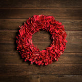 22” red holiday wreath made of natural red integrifolia leaves on a dark wood background.