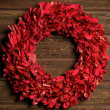 22” red holiday wreath made of natural red integrifolia leaves on a dark wood background.