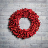 22” red holiday wreath made of natural red integrifolia leaves on a white brick background.